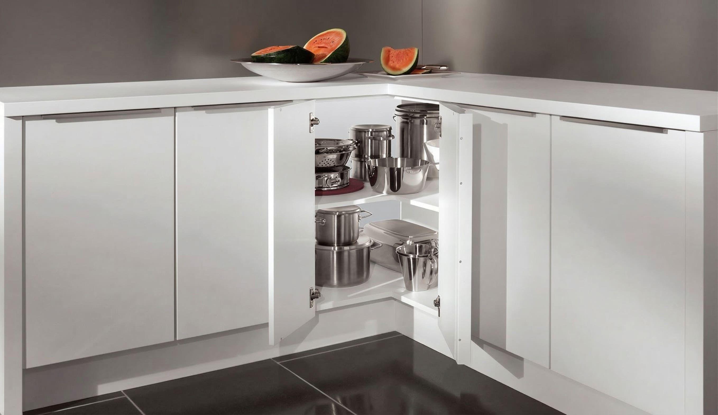 Offener Eckschrank in einer weißen Küche mit mehreren Edelstahl-Töpfen und -Pfannen auf zwei Einlegeböden.