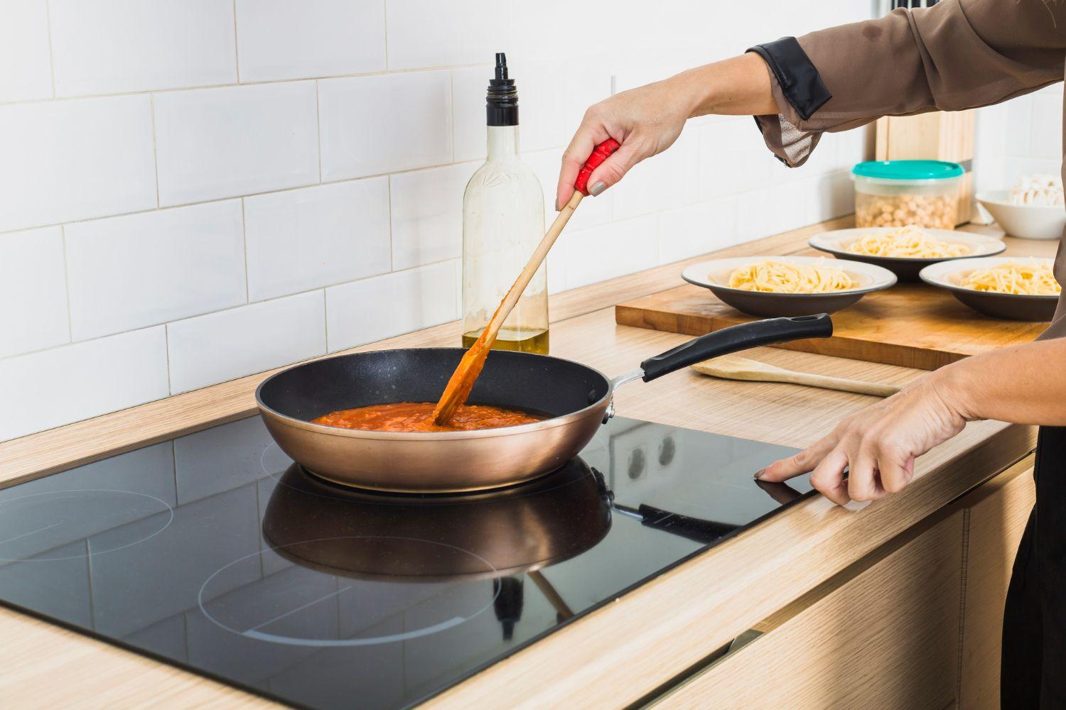 Cerankochfeld mit Pfanne und Tomatensauce in moderner Küche.
