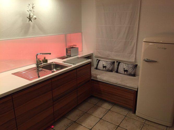 Unsere Referenzen — Walnussküche mit weißer Arbeitsplatte, pinkem LED-Spritzschutz und Smeg-Kühlschrank