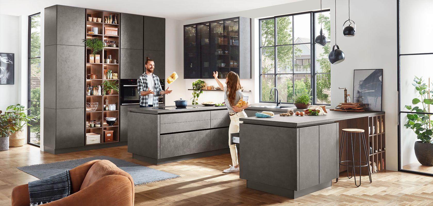 Paar in Beton-Optik-Küche mit Kochinsel, Hochschrank-Vorratsregal und Galerie-Wand