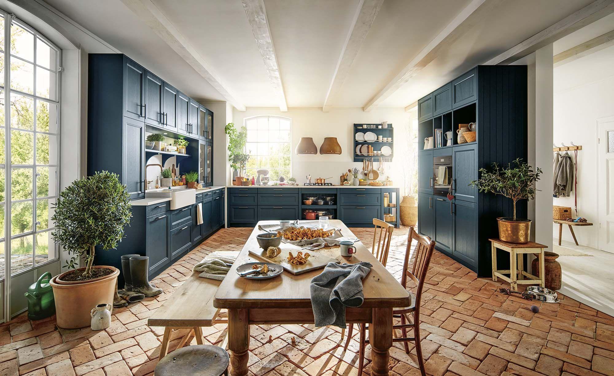 Blaue Landhausküche mit umfangreichen Hängeschränken und langer Holztafel