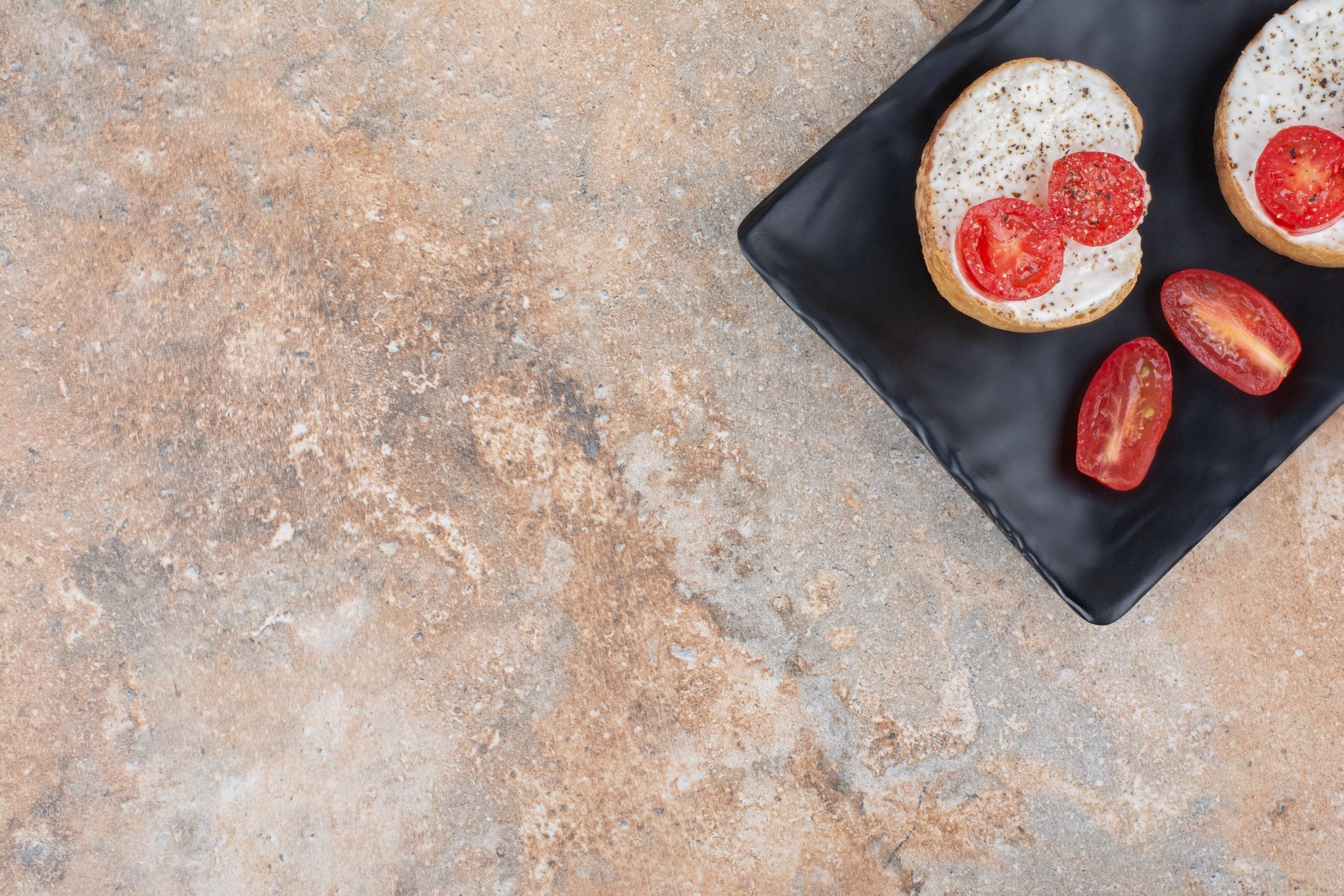 Bruschetta mit Tomaten auf schwarzem Teller auf beiger Naturstein-Arbeitsplatte