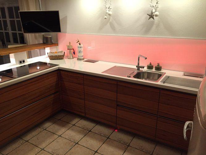 Unsere Referenzen — Walnuss-Küche mit weißer Arbeitsplatte, rosa LED-Spritzschutz und Wand-TV