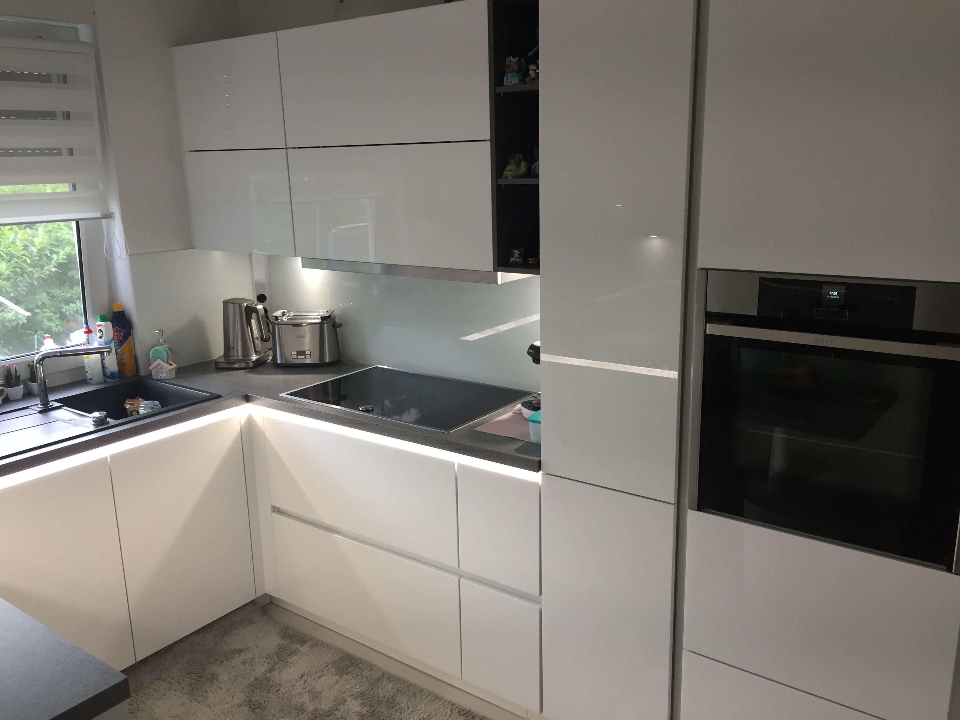 Unsere Referenzen — Weiße Hochglanz-Eckküche mit Hochschrank-Backofen und Grünpflanze