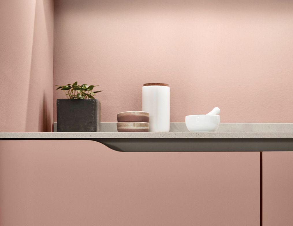 Detail einer rosa Küchenfront mit Griffmulde und Naturstein-Arbeitsplatte