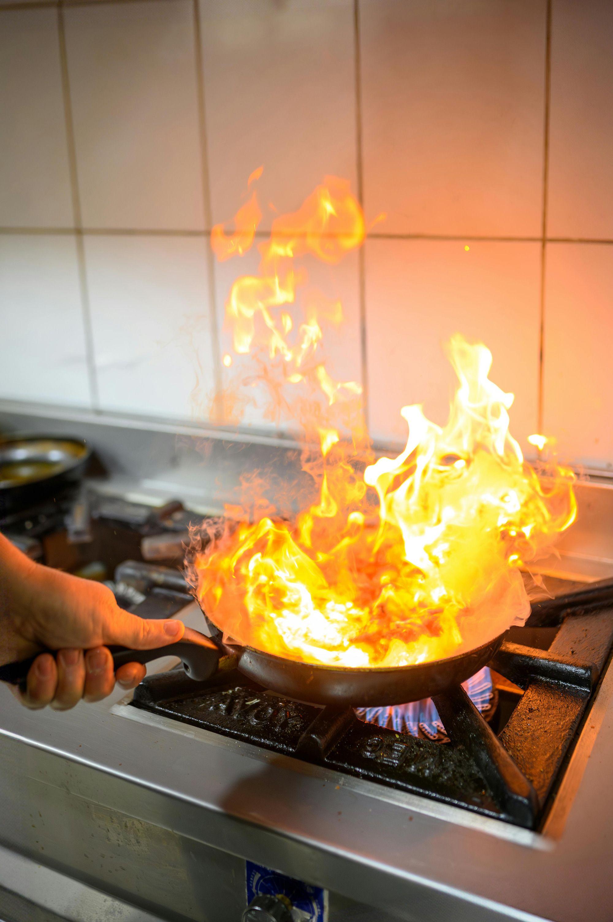 Pfanne mit hoher Flamme auf einem Gasherd in einer Küche, während eine Hand den Griff hält.