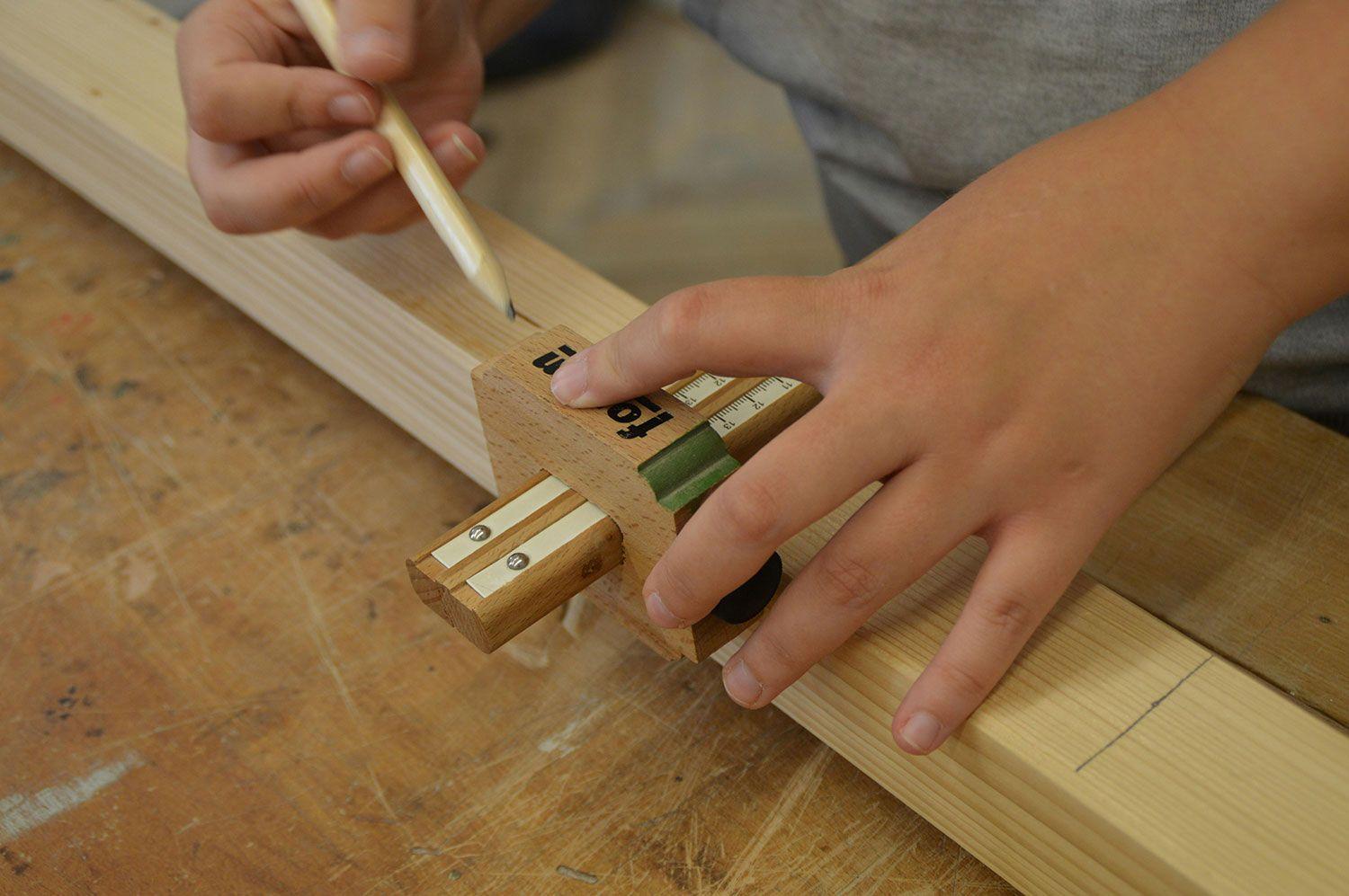 Detail beim Schreinerei-Handwerk: Hände markieren ein Holzbrett mit Bleistift