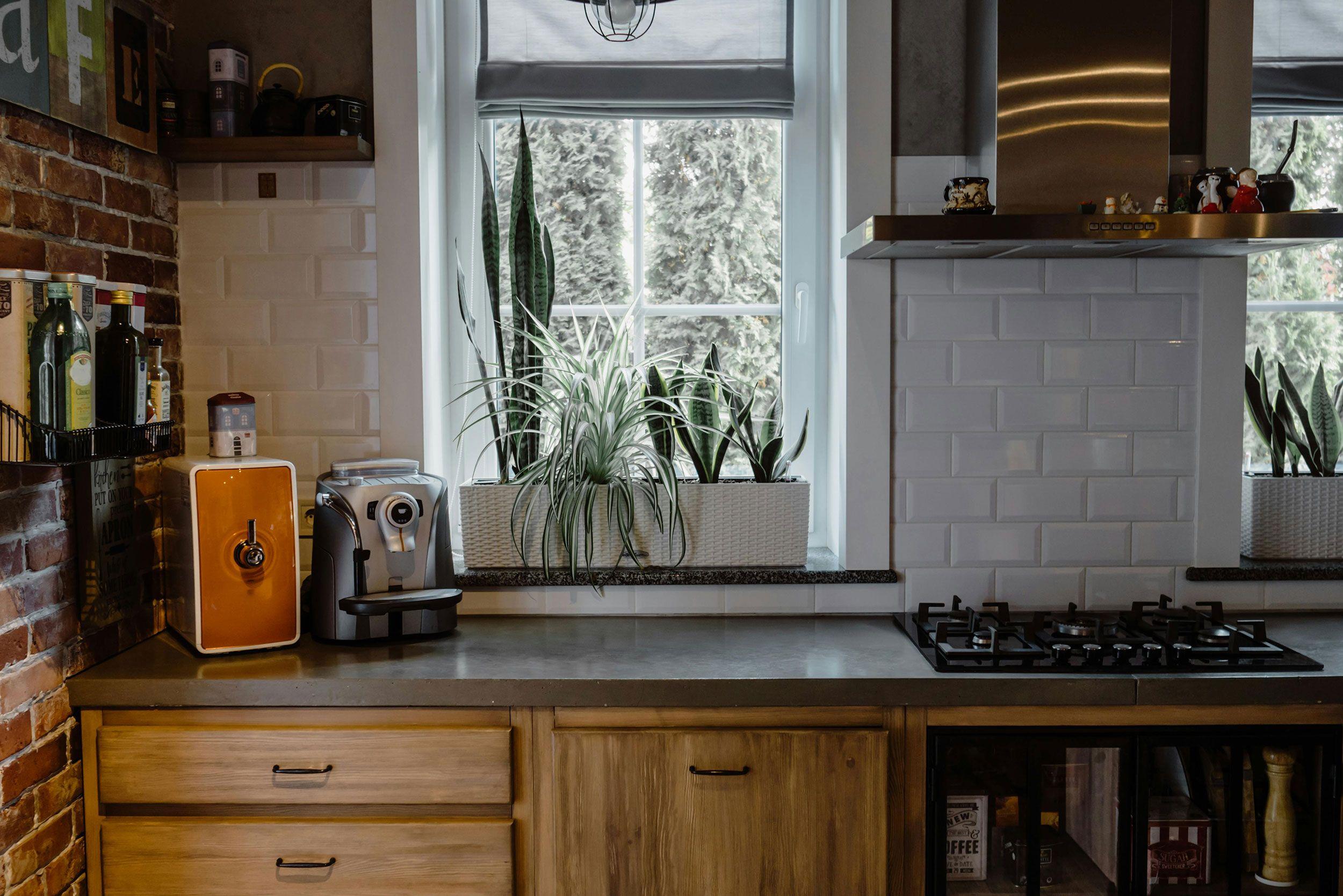 Retro-Küche mit Backsteinwand, oranger Espressomaschine und Pflanzen am Fenster